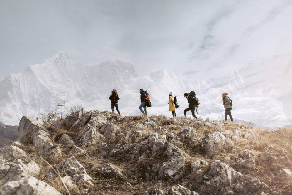 Group of friends hiking and enjoying in a beautiful nature around them. Beautiful snowy mountain peak behind them.
